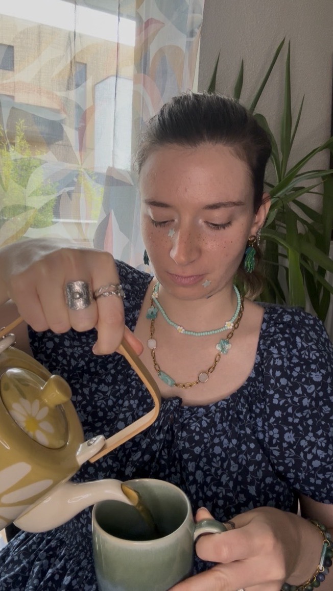 Maëlyss Latour verse du thé dans une tasse, assise près d'une fenêtre